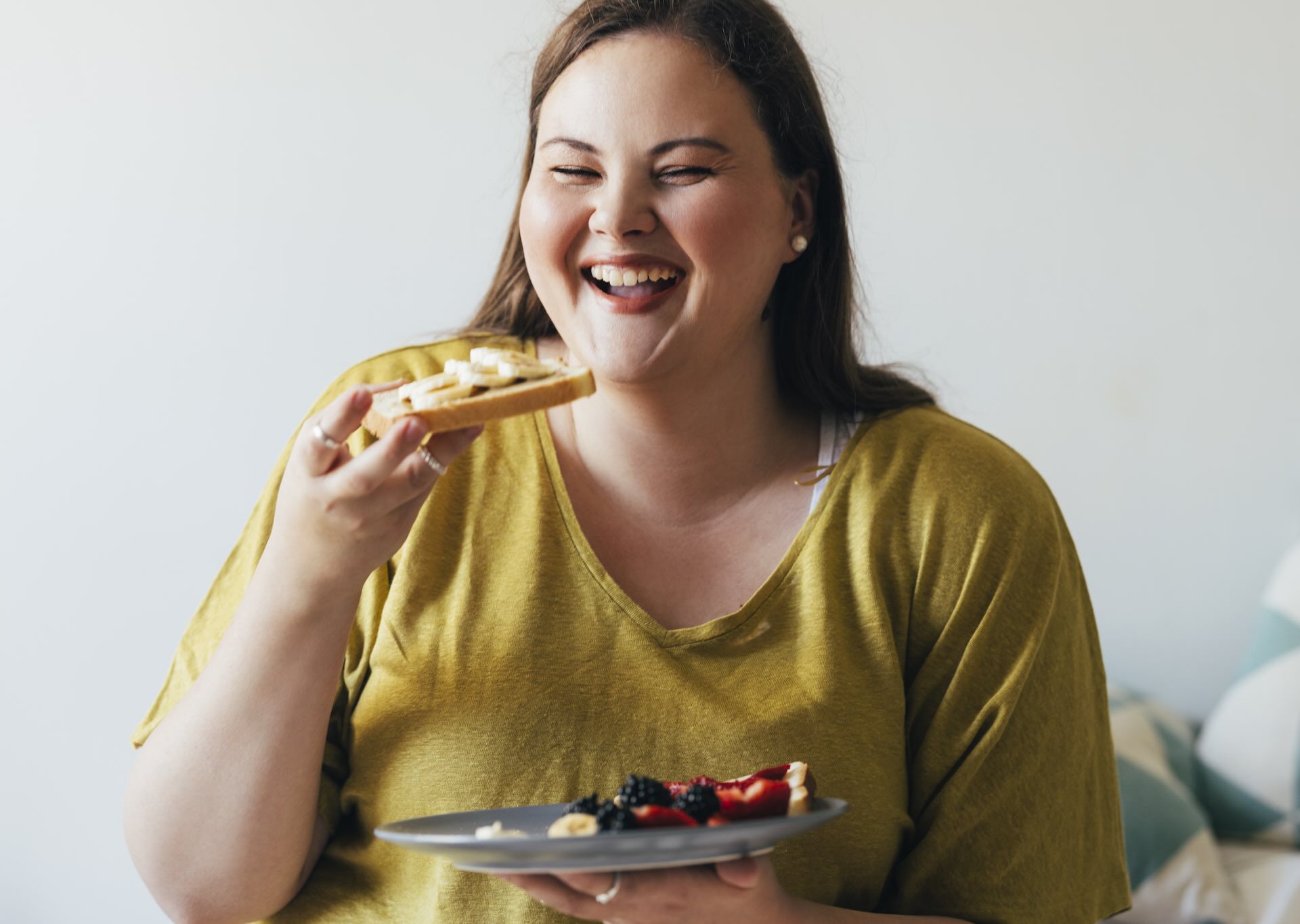 Balanced Hormone Health – December 2025 Blog Images – How-to-Enjoy-Christmas-Dinner-While-on-Semaglutide-or-Tirzepatide Woman smiling while enjoying a healthy meal with fruit on toast