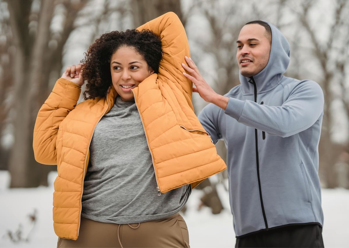 Man and woman exercising outdoors in winter clothing, supporting each other while overcoming winter weight loss struggles.