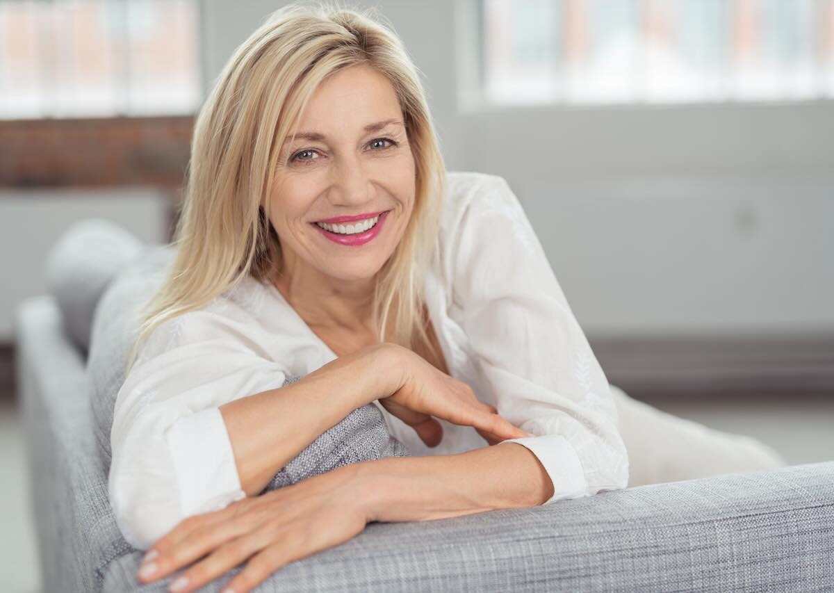 Smiling woman relaxing on a sofa in a bright, comfortable living space.