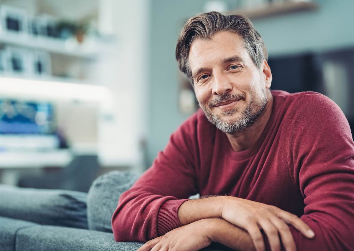 Balanced Hormone Health – February 2026 Blog Images – Why-Enclomiphene-Is-Gaining-Attention-in-Hormone-Therapy Smiling middle-aged man relaxing on a sofa in a modern living room.