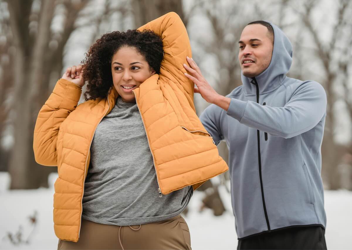 Woman stretching outdoors in winter while a trainer offers gentle guidance.
