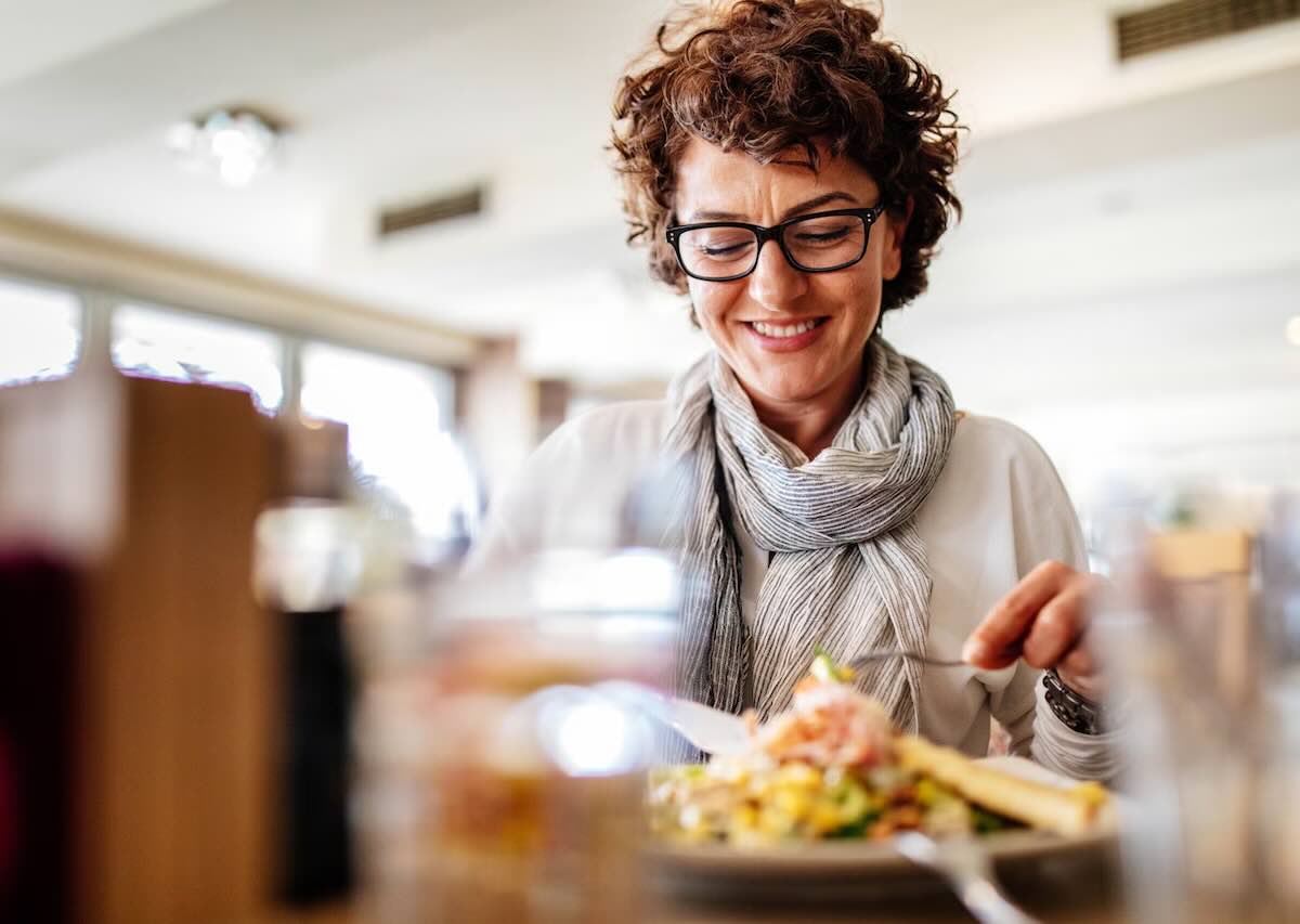 Woman smiling while enjoying a healthy meal at a restaurant.