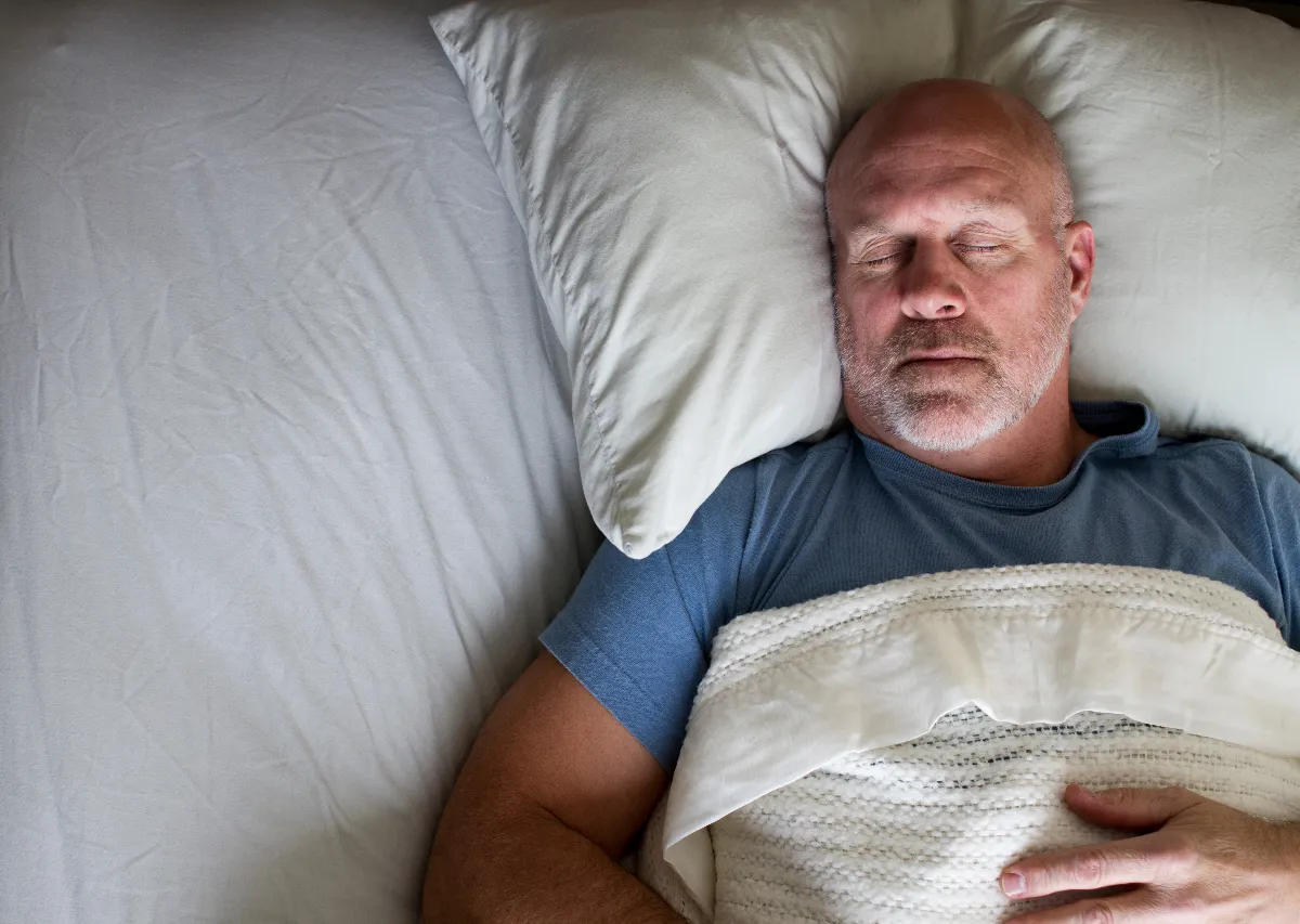 Man sleeping peacefully in bed illustrating the connection between sleep and hormones for better energy and weight loss.