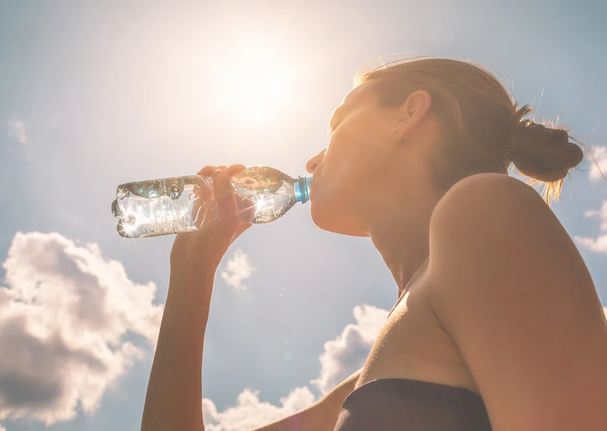 How-Hydration-Impacts-Energy-Metabolism-And-Hormone-Health-In-The-Summer womav drinking a bottle of water in the sunlight