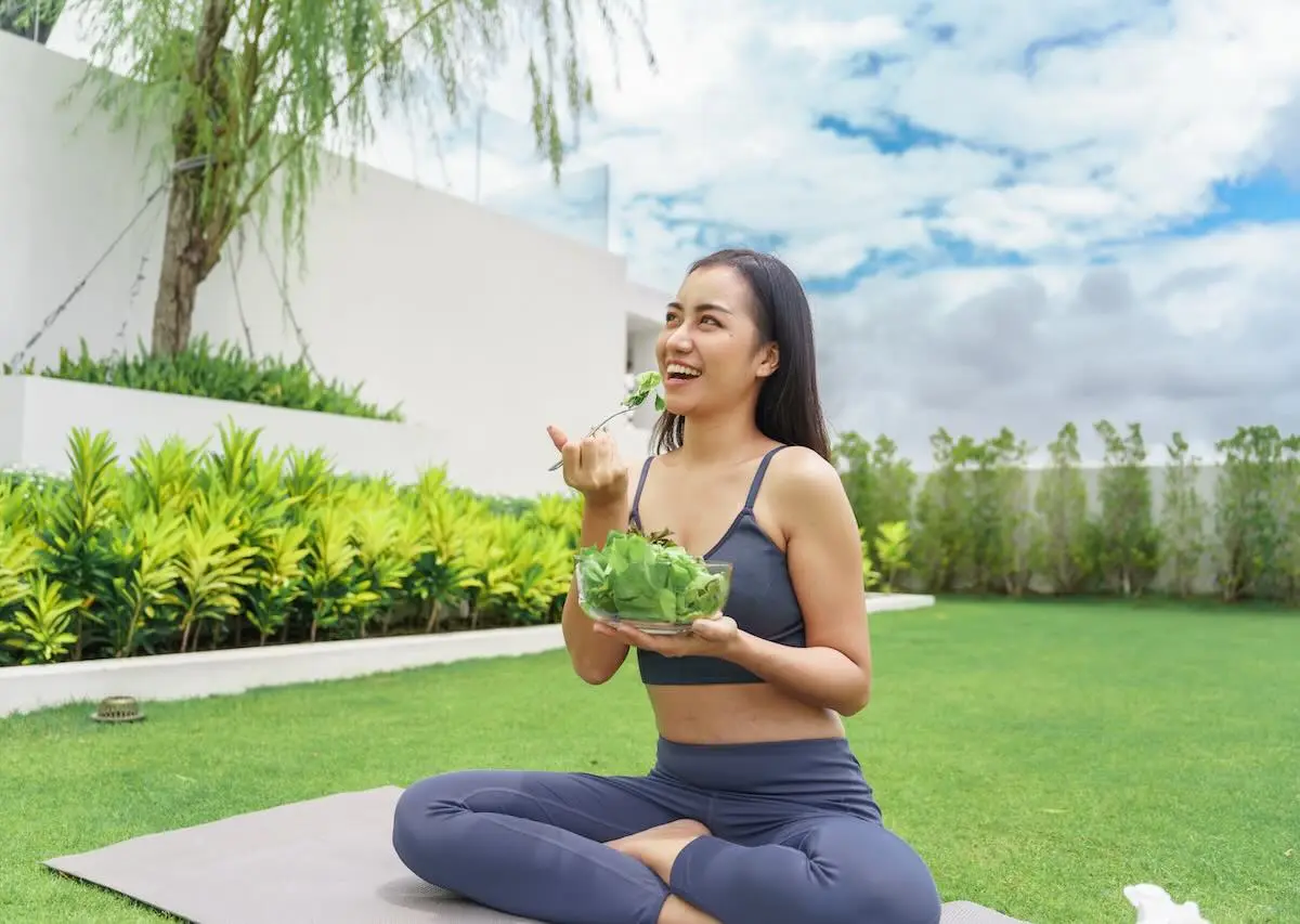 Signs-Your-Metabolism-May-Need-More-Support-Than-Diet-And-Exercise woman sitting in a yoga pose eating a salad outside