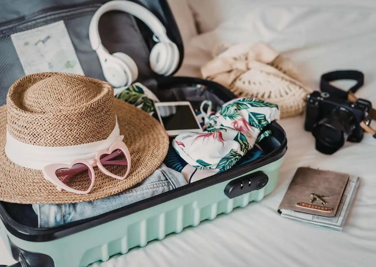 luggage packed with a hat sunglasses and other items sitting on a bed