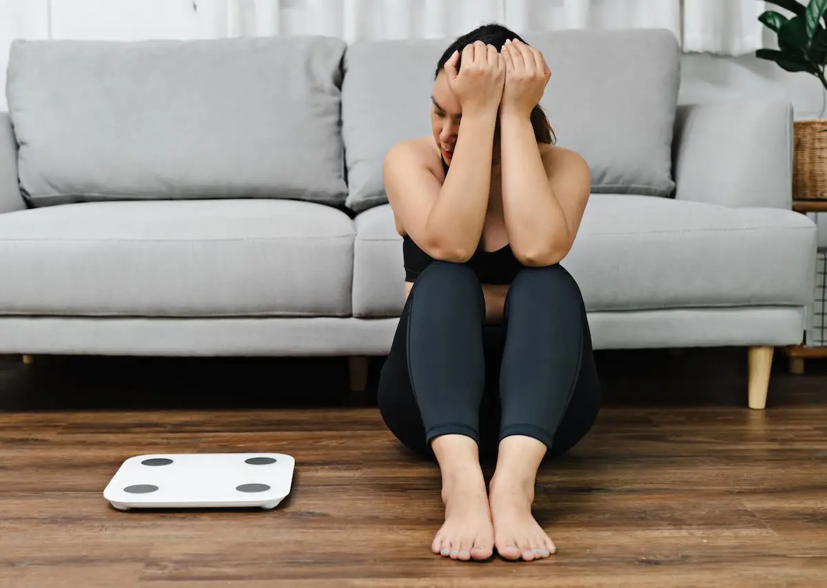 What-Cortisol-Does-To-The-Body-And-Why-Stress-Can-Affect-Weight-Loss woman sitting on the floor staring at her scale in a sad way
