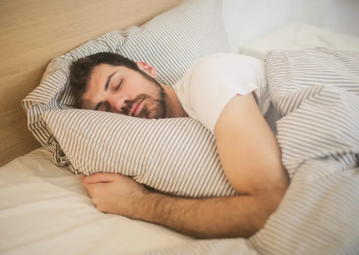 man curled up in bed hugging his pillow as he sleeps