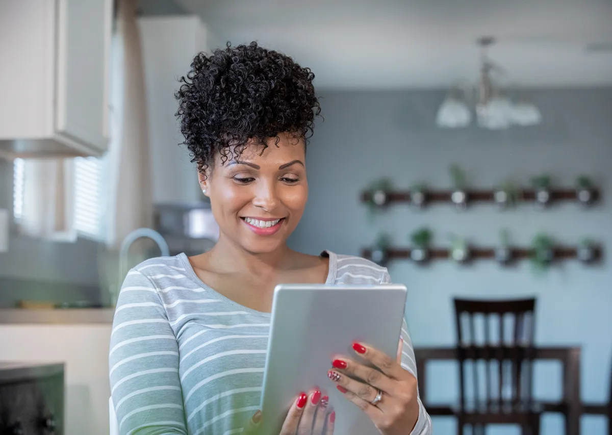 woman looking at a tablet in the kitchen smiling
