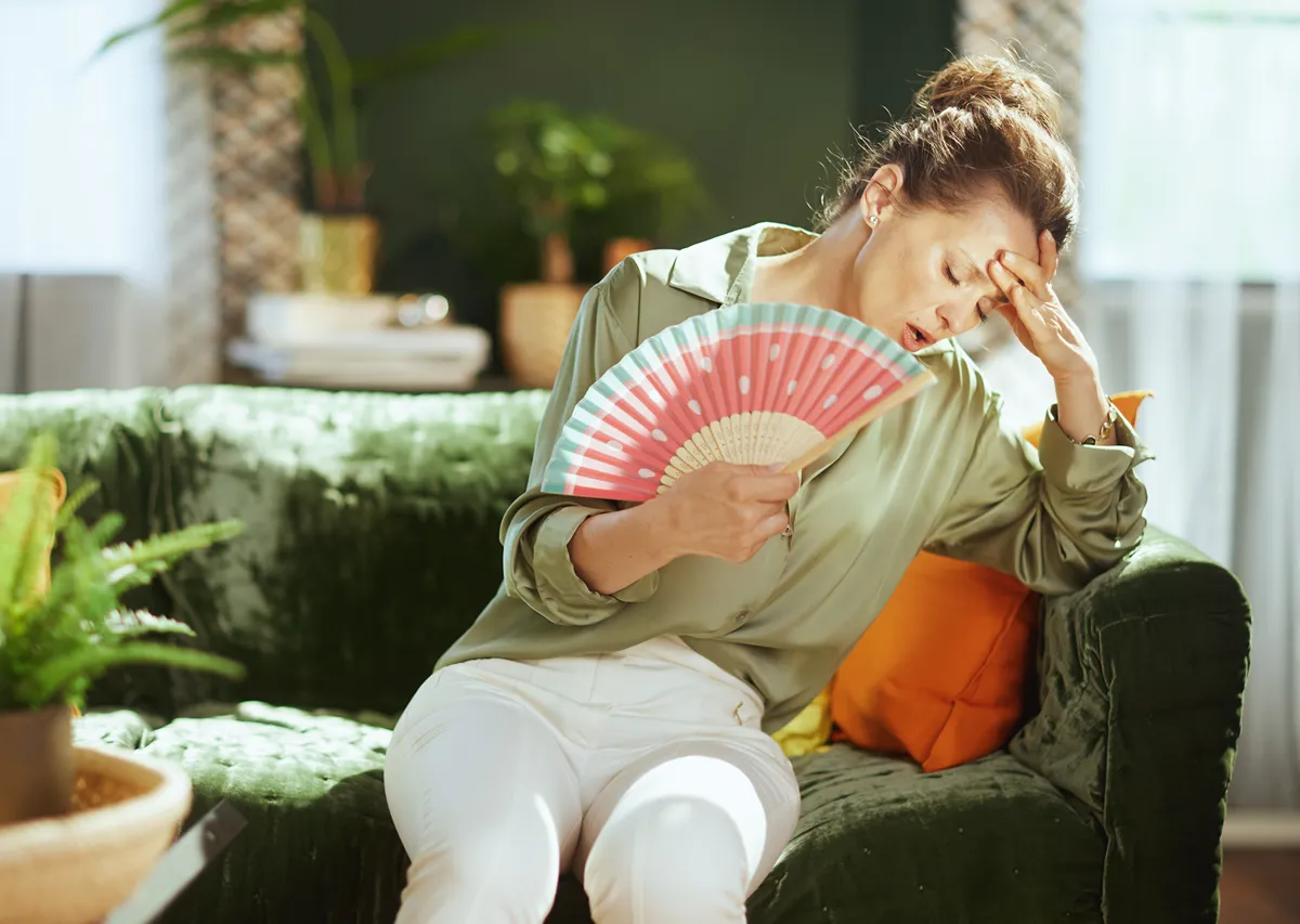 woman sitting on a couch fanning herself.